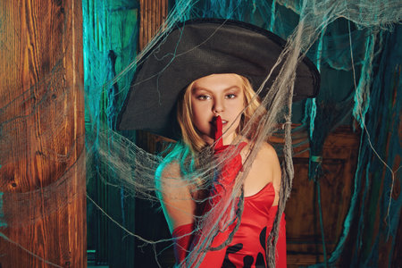Cute happy child girl in a costume of a witch posing in an old house with Halloween decorations....