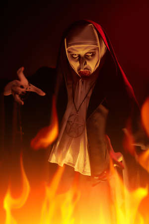 Portrait of evil cursed nun making a threatening gesture on a dark background in light of burning flame. Halloween and Horrors.の写真素材