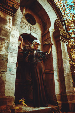 An aristocratic old widow woman with beautiful gray hair and a rich black dress posing in a crypt in...