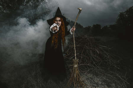 A portrait of an angry witch with a broomstick near the forest. Magic, dark force, spell.の写真素材