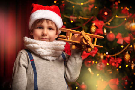 Little boy in the hat of Santa posing holding a wooden plane in a beautiful festive christmas atmosphere. Christmas and New Year concept.の写真素材