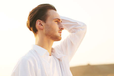 Portrait of a romantic young man in white clothes standing in a desert and looking at sunset.の写真素材