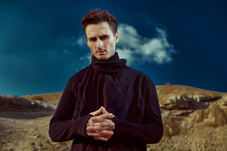 Desert. Portrait of a handsome brunet man in black clothes standing in the desert. Men's beauty,...