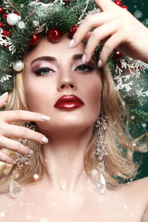 Beautiful happy young woman with a Christmas pine wreath on her head, decorated with Christmas balls, berries and snowflakes. Studio portrait over xmas green background.の写真素材