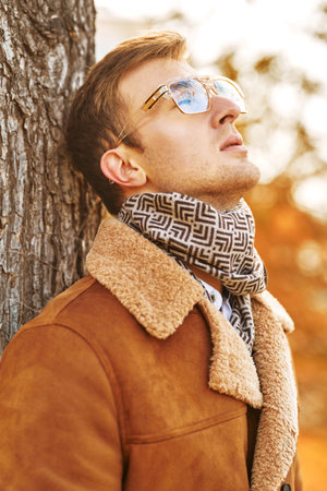 Autumn portrait of an elegant handsome man in glasses and a coat on a background of autumn park.