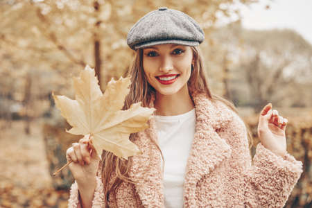 Happy autumn mood. Beautiful young woman walks in the autumn park with yellow maple leaf.の写真素材