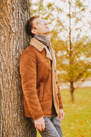 Portrait of an elegant handsome man in glasses and a coat walking in the autumn park. Seasonal beauty, men's fashion.の写真素材