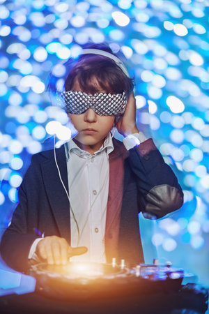 Christmas and New Year kid's party. Cool DJ boy in headphones on a background of festive lights....
