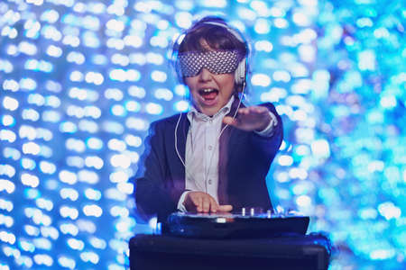 Cool emotional DJ boy in headphones on a background of festive lights. Disco. Christmas and New Year kid's party.の写真素材