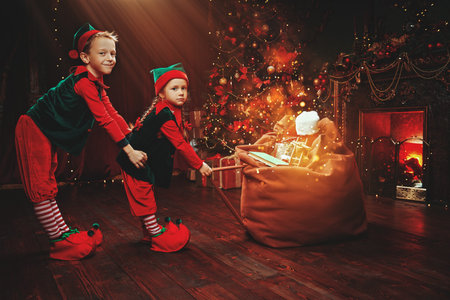 Christmas tale. Little elves carry a heavy big bag of presents. They are in a house with a beautiful...
