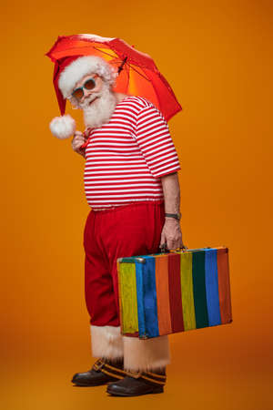 Jolly funny Santa Claus goes on vacation. Christmas Holidays, tourist trips to hot tropical countries. Bright yellow background. Copy space.の写真素材