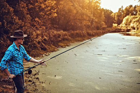Young man is fishing on the lake on a warm autumn day. Active lifestyle, outdoor recreation.