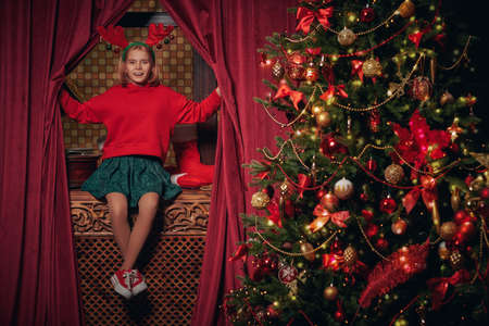 Merry Christmas and Happy New Year! Funny joyful girl with deer horns on her head celebrates Christmas at home. Beautiful festive decoration.の写真素材