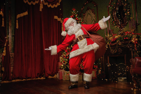 Santa Claus brought gifts for Christmas. He stands in a night room with beautiful Christmas tree and...