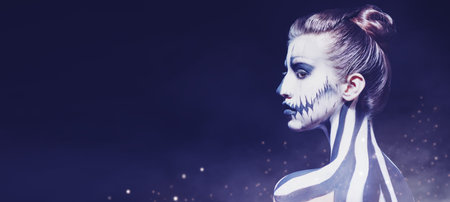 Portrait of a beautiful young woman with Halloween skeleton makeup over black background. Pumpkin...