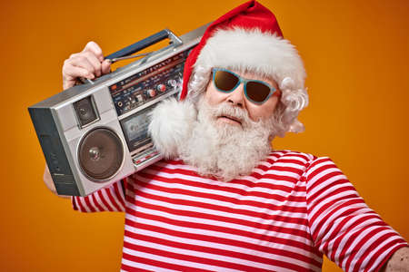 Cool DJ Santa Claus in sunglasses holds tape recorder on a bright yellow background. Christmas songs and music. New Year party.の写真素材
