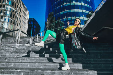Bright colors concept. Modern girl in colorful clothes poses in a big city against the backdrop of skyscrapers. Fashion shot.の写真素材