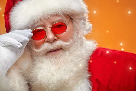Close-up portrait of a modern Santa Claus in red sunglasses. Yellow background with twinkling stars.の写真素材