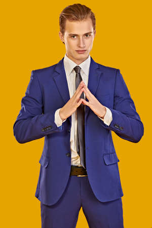 Portrait of a handsome young man in elegant blue suit on a yellow background. Male beauty, fashion. Business style.の写真素材