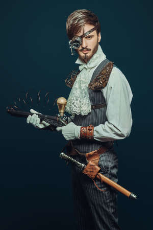 Portrait of a handsome noble man with steampunk gadgets and a gun on a dark blue background. Steampunk concept.の写真素材