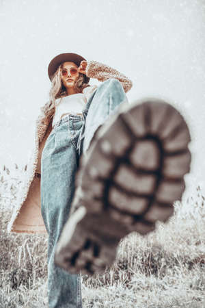 Attractive young woman in fashionable winter clothes confidently steps towards the camera. Winter landscape with snowfall. Winter fashion.の写真素材