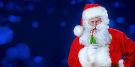 Funny serious Santa Claus drinks soda on a dark blue background. Entertainment concept. Merry Christmas and Happy New Year! Copy space.の写真素材