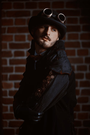 Steampunk world. Portrait of a stylish steampunk man in a coat and bowler hat on a brickwall...