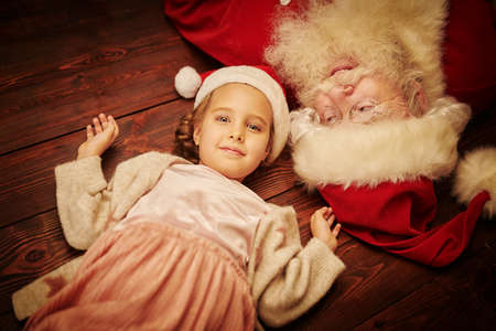 Portrait of a happy little girl and Santa Claus having fun on a floor. Merry Christmas and Happy New Year!の写真素材