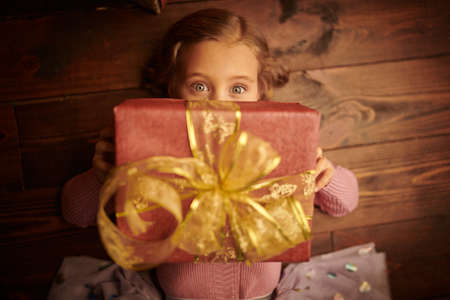 Close-up portrait of a lovely little girl lying on a wooden floor with a gift box. Merry Christmas and Happy New Year!の写真素材