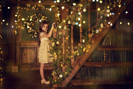 Happy little girl celebrates Christmas in a house beautifully decorated with spruce garlands and New Year's toys. The atmosphere of magic, lights and sparkle is around.の写真素材
