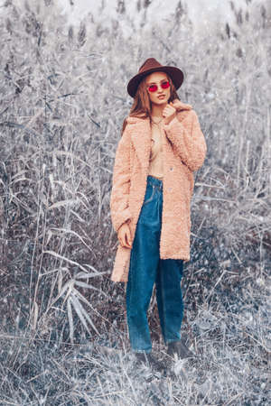 Winter fashion. Full length portrait of a beautiful young woman in trendy clothes posing next to the reeds on the background of the winter landscape.の写真素材