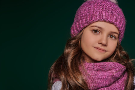 Portrait of a cute smiling girl child wearing knitted hat and a scarf on a dark green background. Kid's fashion. Winter clothes. Merry Christmas and Happy New Year!の写真素材