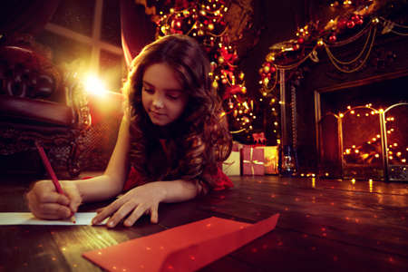 Christmas and New Year holidays. Happy child girl dreams of a gift and writes a letter to Santa Claus, lying next to a beautiful Christmas tree.の写真素材