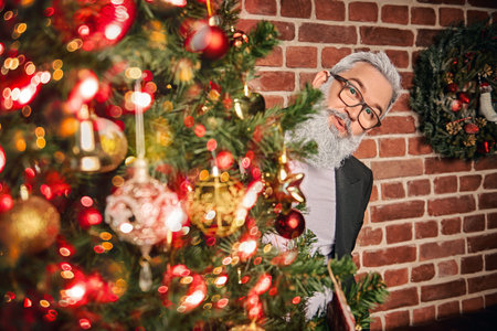 Merry Christmas and Happy New Year! Portrait of a modern Santa Claus looking out from behind the Christmas tree. Loft interior with New Year decorations.の写真素材