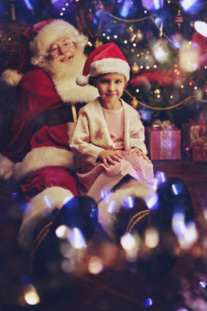 Santa Claus is playing with a little girl at home next to a Christmas tree. Merry Christmas and Happy New Year!の写真素材
