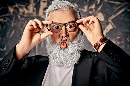 Funny surprised man with a gray beard looks through glasses with big eyes. Vision and glasses concept.の写真素材