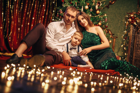 Joyful parents sit with their beloved son in a beautiful cozy Christmas atmosphere at home. Happy family holiday.の写真素材