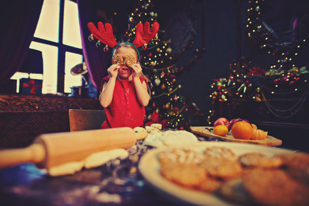 Funny little girl bakes cookies for Christmas. Happy family holidays. Child at home beautifully decorated for Christmas.の写真素材
