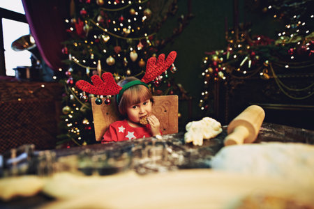 Cute little girl eats cookie and helps her mother to bake cookies for Christmas. Child at home beautifully decorated for Christmas. Happy family holidays.の写真素材