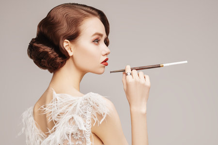 Beautiful chic woman in a luxury white dress smoking a cigarette in the mouthpiece. Evening makeup...