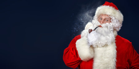 Christmas and New Year. Portrait of a funny Santa Claus smoking a pipe. Studio portrait over dark blue background. Copy space.の写真素材