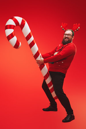 Fat sexy bearded hipster man wearing deer horns and red sweater smiling at camera and flirting. Red background.の写真素材