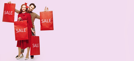 Holiday sale. Full length portrait of a couple fashionable young people posing with purchases on a lilac background with copy space. Shopping on holidays.の写真素材