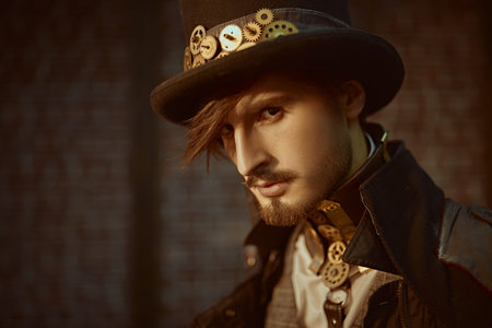 Close-up portrait of a stylish steampunk man in a coat and top hat on a brickwall background. Steampunk world.の写真素材