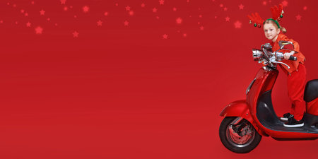 Cute little girl in deer horns rides a red scooter carrying gifts for children. Festive red background with stars. Copy space.の写真素材