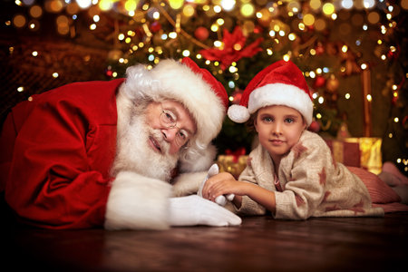 Santa Claus is playing with a little girl at home next to a Christmas tree. Merry Christmas and...