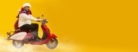 Happy fat man in Santa Claus hat rides a red scooter carrying gifts for Christmas and New Year. Bright yellow background with snow and copy space. Modern hipster Santa Claus.の写真素材