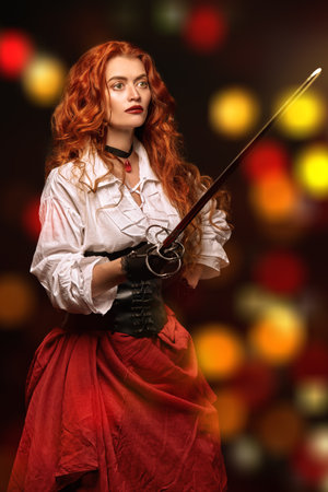 Beautiful red-haired woman with a battle epee (rapier) on a black background with lights. Historical reconstruction of the 16-17th centuries.の写真素材
