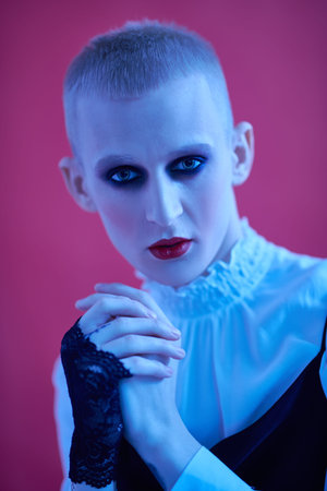 Avant-garde fashion. Portrait of a young man with women's makeup and women's clothing posing in blue...