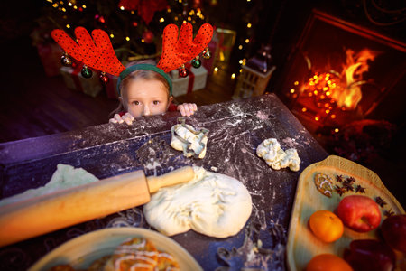 Funny little girl bakes cookies for Christmas. Happy family holidays. Child at home beautifully decorated for Christmas.の写真素材